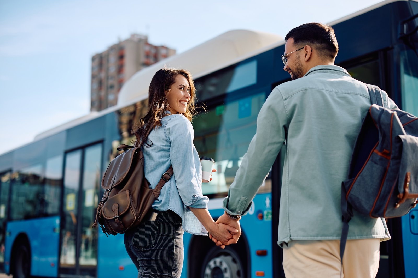 happy couple talking while holding hands at city bus station.